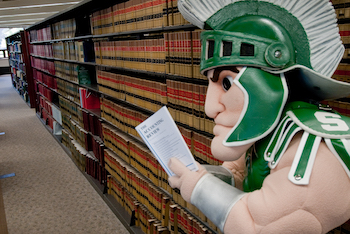 Sparty reading in the library